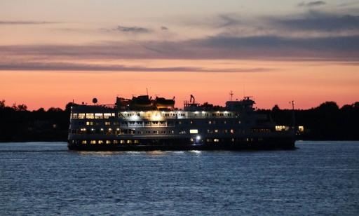 Under the pink and purple sunset sky, golden light shines from the many windows of a ship.