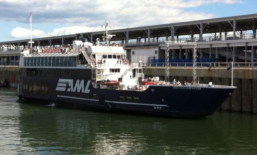 A blue boat approaches the pier. On the top, above the windows, the word "excursions" is written in white on a red sign.