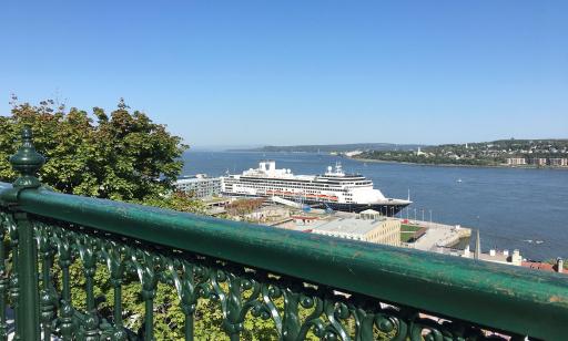 View from high up, behind a green railing, of the river and a large cruise ship moored at the wharf. 