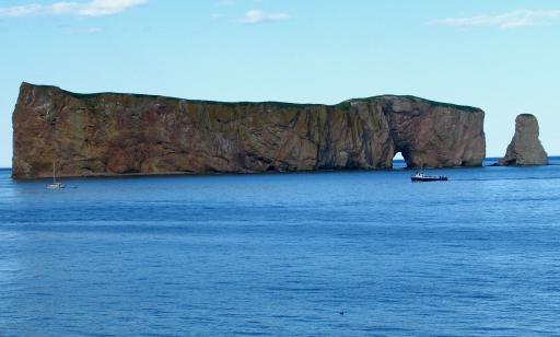 A small navy and white motorboat sails past a huge rock with sheer sides and a hole in the middle.