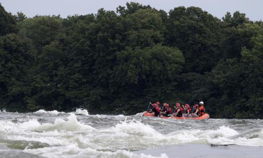 Ten people wearing helmets paddle an inflatable boat through rough waters.