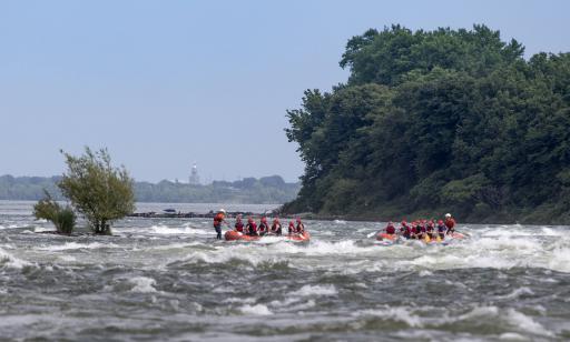 People paddle an inflatable boat through rough water toward another inflatable boat stopped on a shoal.