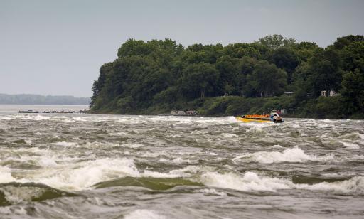 Un homme pilote un bateau à moteur à jet, avec un guide et neuf passagers à bord, dans des eaux très agitées près d’une île.