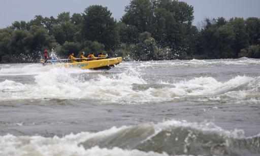 People on a jet boat headed against the current on rough waters, in front of a wooded island.