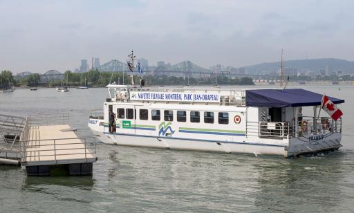 A white ship approaches a wharf. In the distance, an amusement park, skyscrapers and a mountain can be seen.