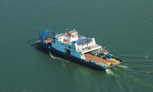 Aerial view of a flat blue and white boat, loaded with cars and trucks, crossing the water.