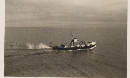 A boat fitted with a cabin, fog horns, and tires around its hull sails across a wide stretch of water.