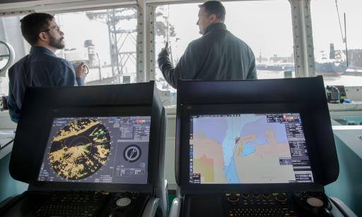 Two men talk in front of the large windows of the wheelhouse. Two colour screens are behind them.