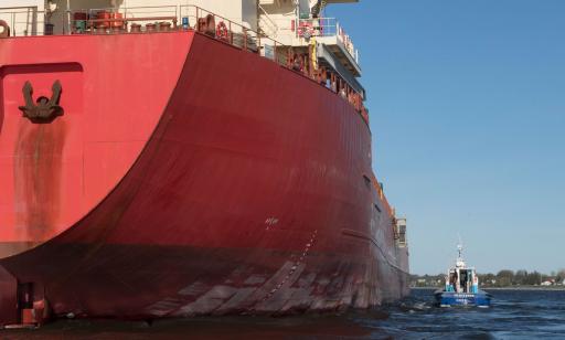 A small blue and white boat parallel to the starboard side of a large orange cargo ship.