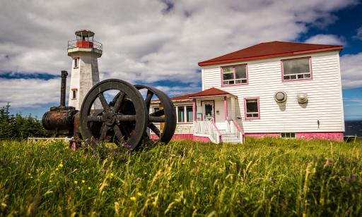 View of a house, a rusty black cannon with large wheels and a white octagonal tower topped with a red lantern.