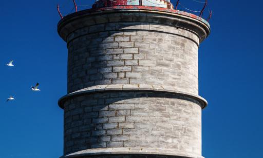 Under a clear blue sky, we can see a grey tower encircled by several rings and topped with a red lantern.