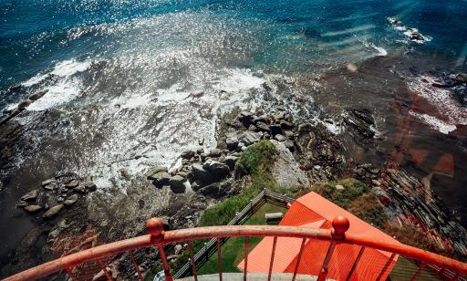 View from the lantern platform of a red roof and waves smashing against the rocks. 