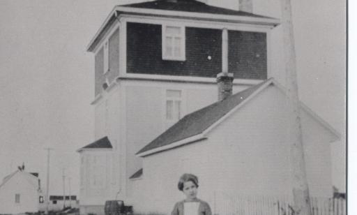 A young girl stands in front of a three-story house with a lantern in the middle of the roof.