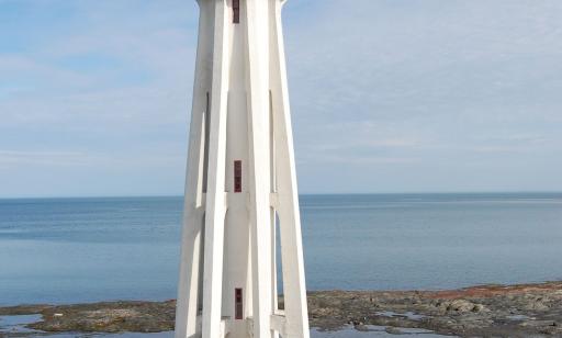 A large white lighthouse with tall narrow windows, topped with a red lantern, stands near the shore.