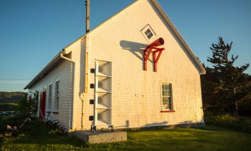 A rectangular device that resembles a loudspeaker sits next to a building with a red fog horn on its side.