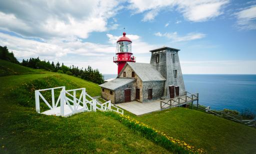 Two lighthouses look out over the sea. One is all red, while the other is attached to a house and covered in cedar shingles.