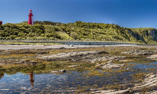 At low tide, a lighthouse at the top of the steep shore is reflected in a tidepool.