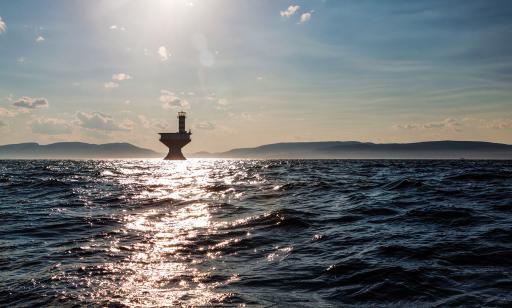 A lighthouse stands on an hourglass-shaped metal structure in the middle of a wide stretch of water.