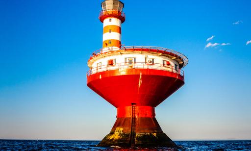 A red and white lighthouse sits atop an hourglass-shaped red metal structure that emerges from the water.