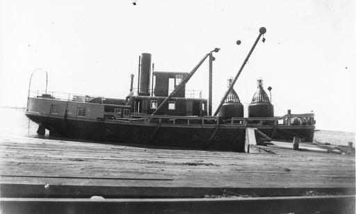 A steamboat fitted with hoists moored at a dock. Two gas buoys sit on its front deck.