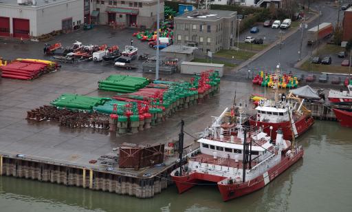 Red and white boats moored at a wharf stacked with buoys of different shapes and colours.