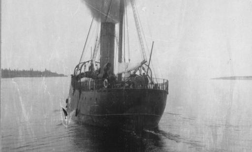 Smoke pours out of the central stack of a steamboat. Lanterns are set atop its two masts.