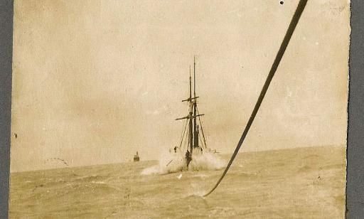 A partially submerged cable tied to a boat with furled sails. The boat is leaving a large wake behind it.