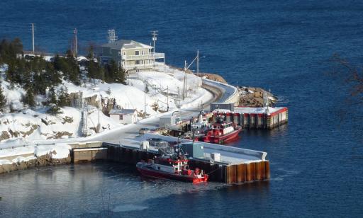 Aerial view of a two-story house by the shore and three red and white pilot boats moored at a wharf.