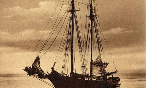 Yellowed black and white photo of a wooden schooner with furled sails anchored in the middle of the river.