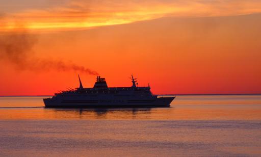 Thick smoke rising from a ship's stack stands out against the bright sky at dusk. 