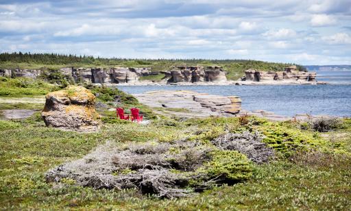 Deux chaises de parterre rouges sont placées face aux falaises grises, couvertes en partie de lichen jaune, bordant la mer.