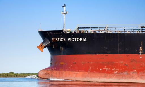 A large ship casts a wake in front of its prow as it sails along the channel near an island.