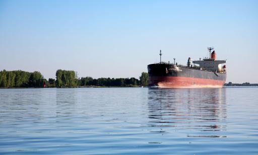 A large ship with a complex cargo pipe system on its deck leaves a wake as it sails past an island.