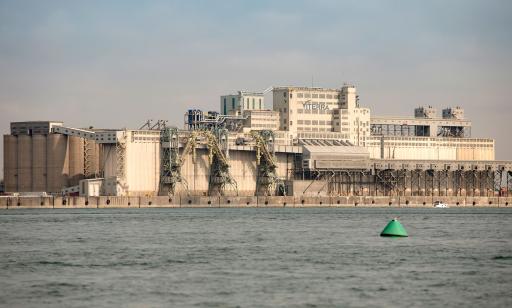 On voit le fleuve et, au loin, des installations portuaires comptant un grand nombre d’immenses silos en béton et des tours.