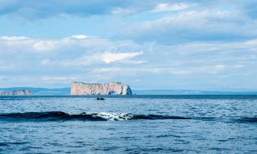 A personal watercraft drives over a wide stretch of water in front of a sheer rocky island with a large hole through it.